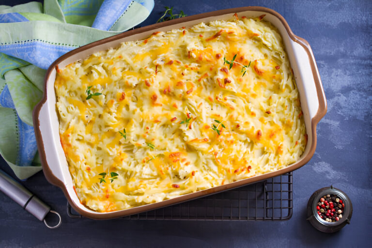 A baked dish of cheesy potato casserole garnished with fresh thyme, placed on a cooling rack next to a spice container.