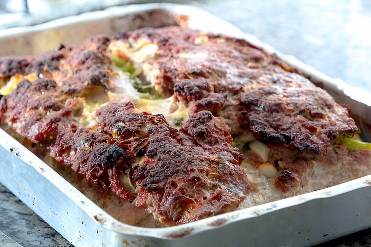 A freshly baked meatloaf in a silver tray showing a crispy top and visible vegetables.