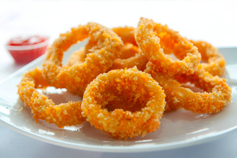 A plate of golden-brown onion rings served with a side of ketchup.