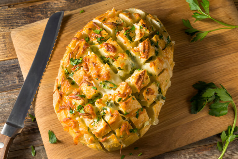 A beautifully baked and sliced cheesy bread on a wooden cutting board, garnished with chopped herbs.