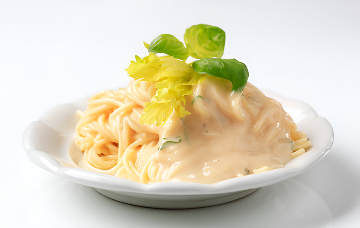 A plate of pasta topped with a creamy sauce and garnished with fresh green leaves and a sprig of celery.