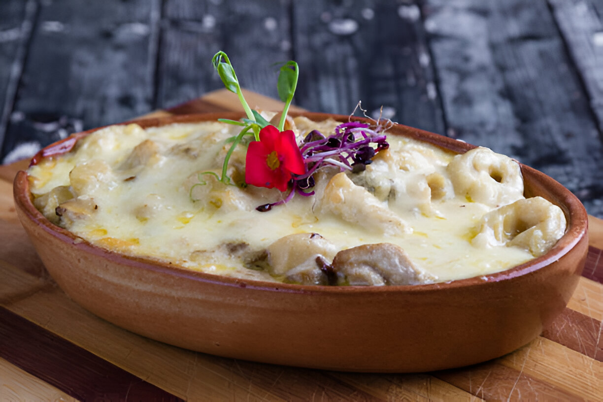 A baked dish with creamy cheese, small pasta, and garnished with a flower on a wooden surface.