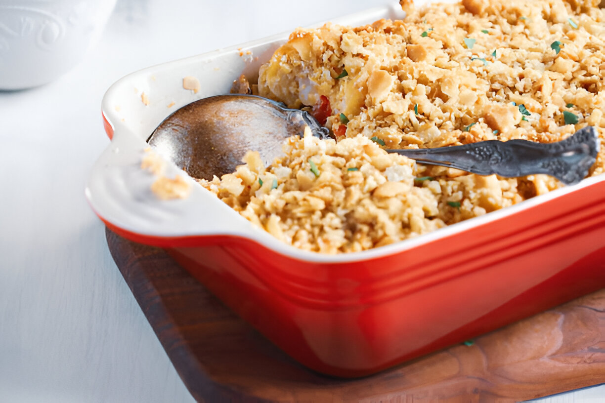 A red baking dish filled with a baked casserole topped with golden breadcrumbs and a serving spoon.