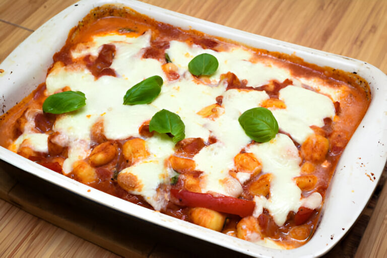 Baked gnocchi with melted mozzarella and fresh basil leaves on top.