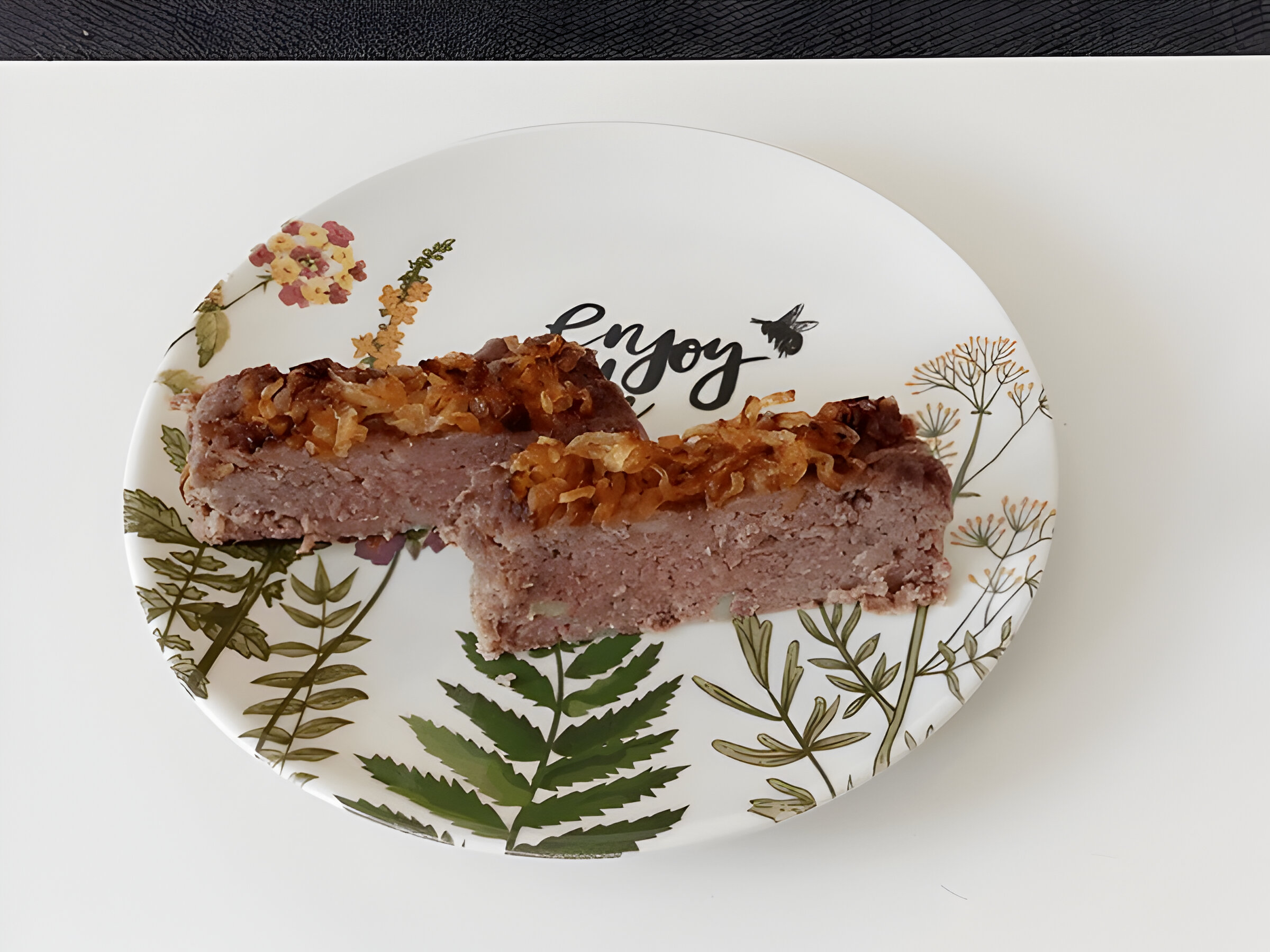 Two pieces of meatloaf on a decorative plate with the word 'Enjoy' and floral patterns.