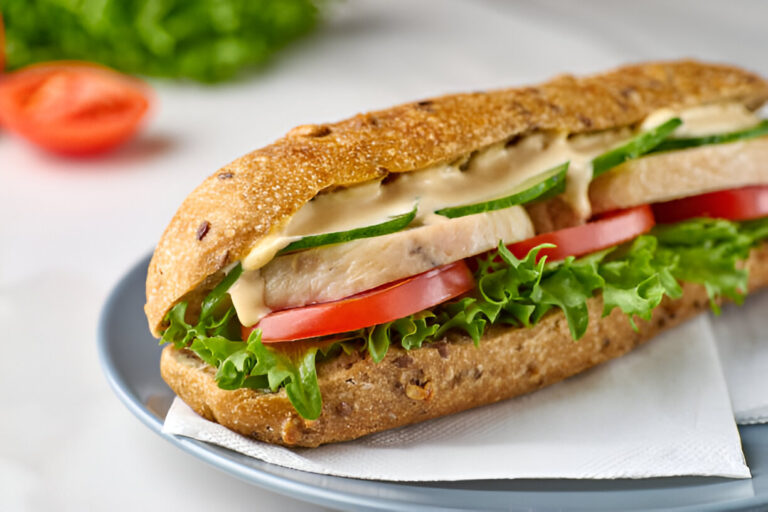 A delicious sandwich made with a multigrain bread, filled with lettuce, tomato, cucumber, and sliced chicken, served on a plate.