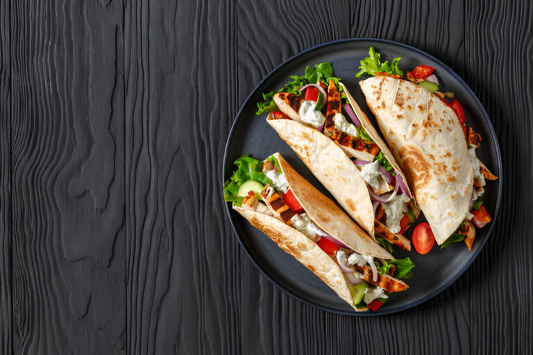 A plate of fresh wraps filled with grilled chicken, lettuce, tomatoes, and a creamy dressing, set on a dark wooden table.