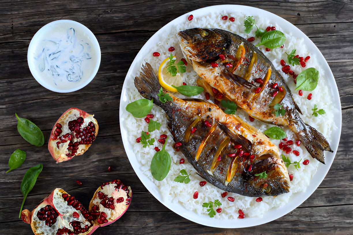 A beautifully plated dish of grilled fish served on a bed of white rice, garnished with pomegranate seeds and fresh herbs.