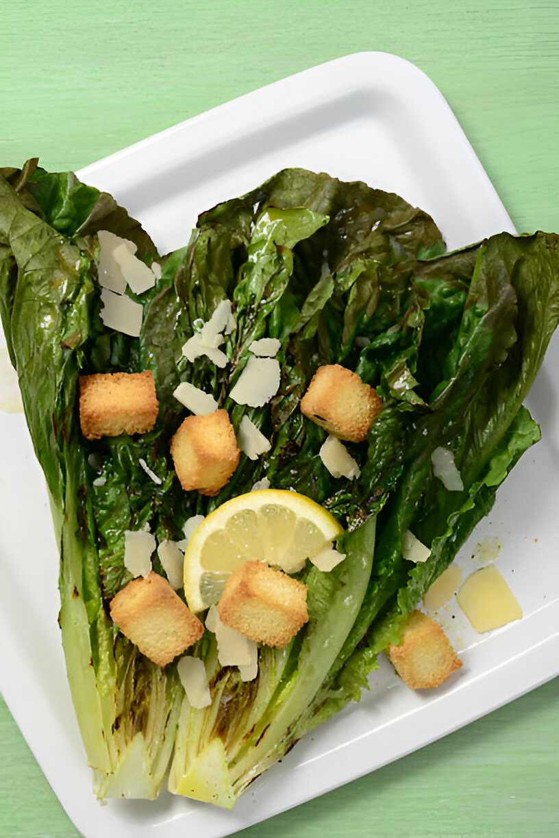 A fresh romaine lettuce garnish topped with croutons, lemon slices, and shaved cheese on a white plate.