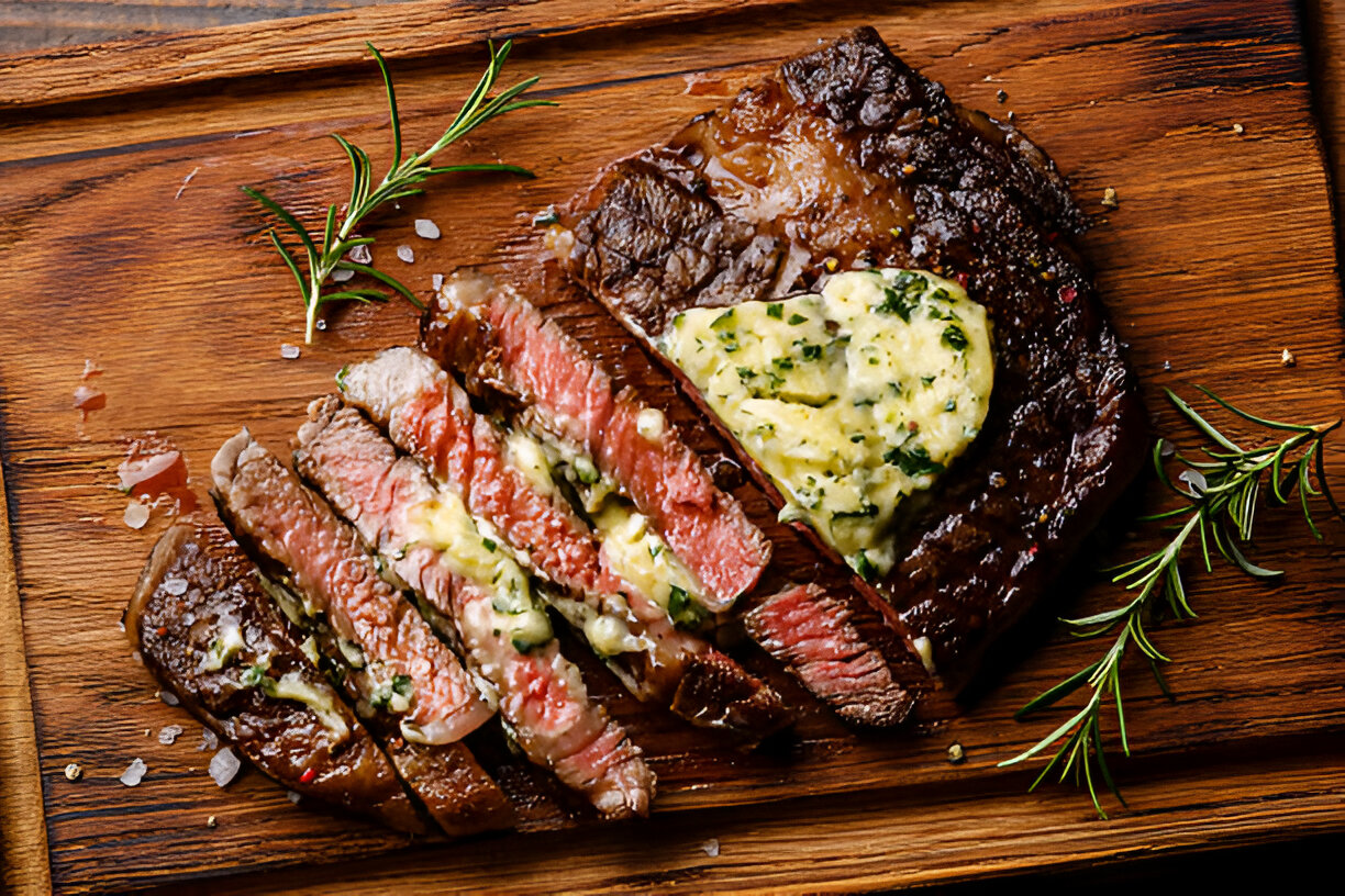Sliced juicy steak topped with garlic herb butter on a wooden cutting board