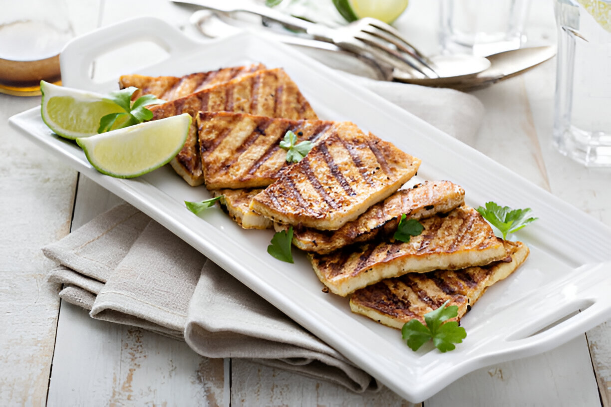 Grilled sliced tofu on a white platter with lime wedges and garnish
