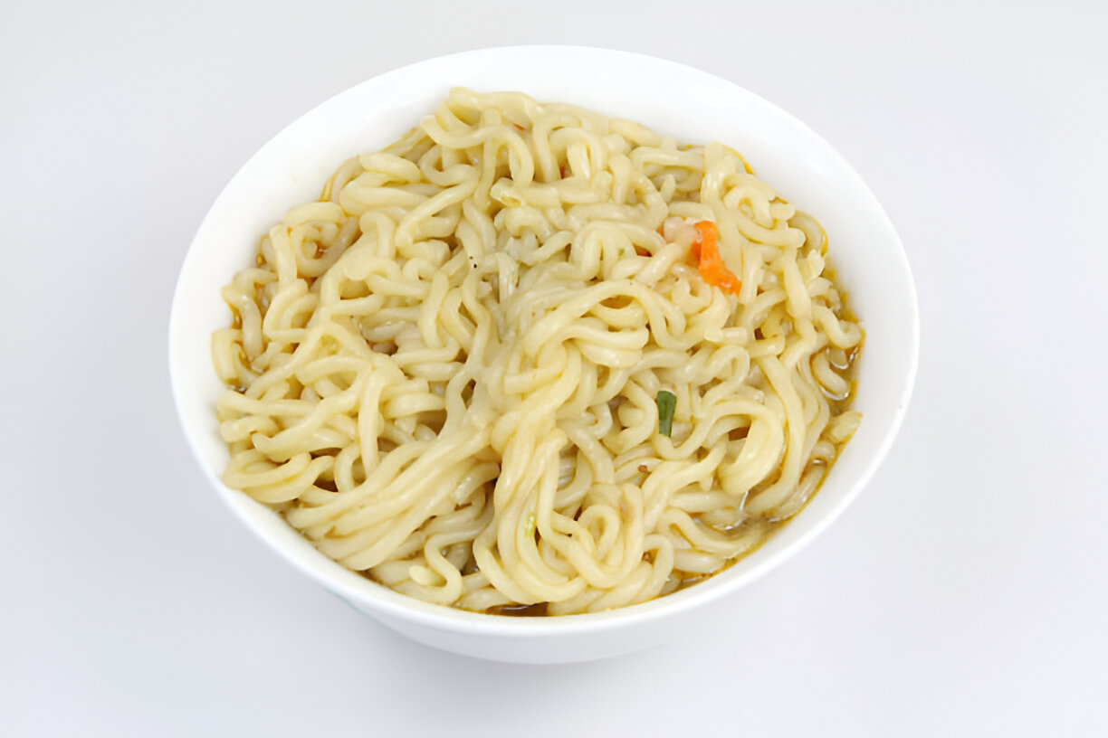 A bowl of cooked noodles with a light brown broth and some small pieces of vegetables.