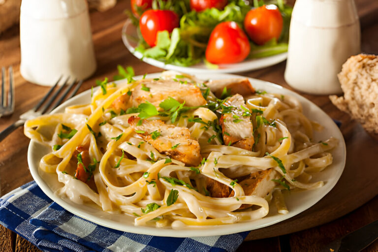 Plate of creamy chicken fettuccine pasta with fresh herbs and grilled chicken, served with a side of salad and bread.