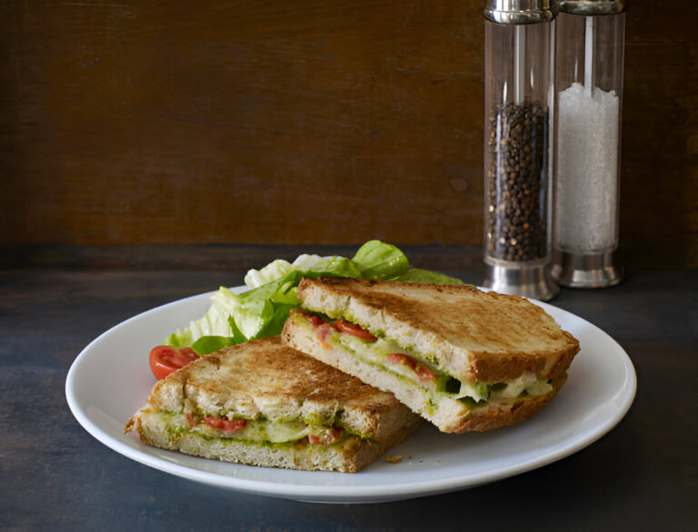 Two halves of a grilled sandwich with lettuce and tomato on a white plate, with salt and pepper shakers in the background.