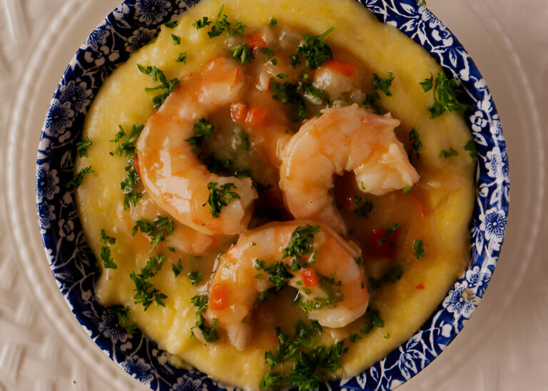 A bowl of shrimp and grits topped with parsley on a decorative plate.
