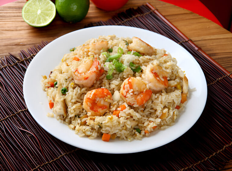A plate of shrimp fried rice garnished with green onions, served with lime slices in the background.