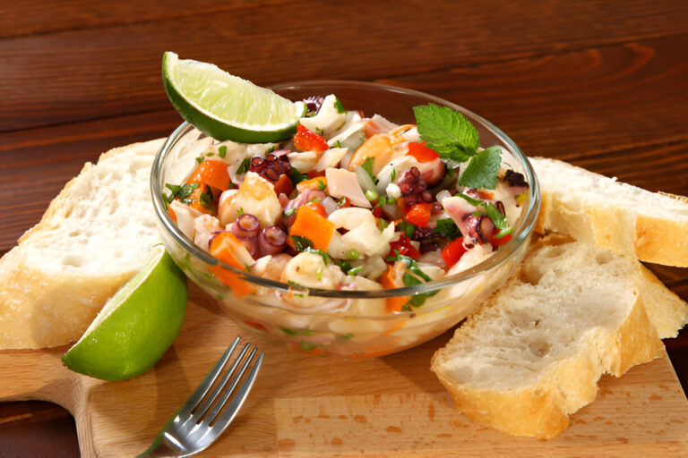 A vibrant seafood salad with octopus, shrimp, and vegetables, served in a glass bowl with lime and bread on the side.