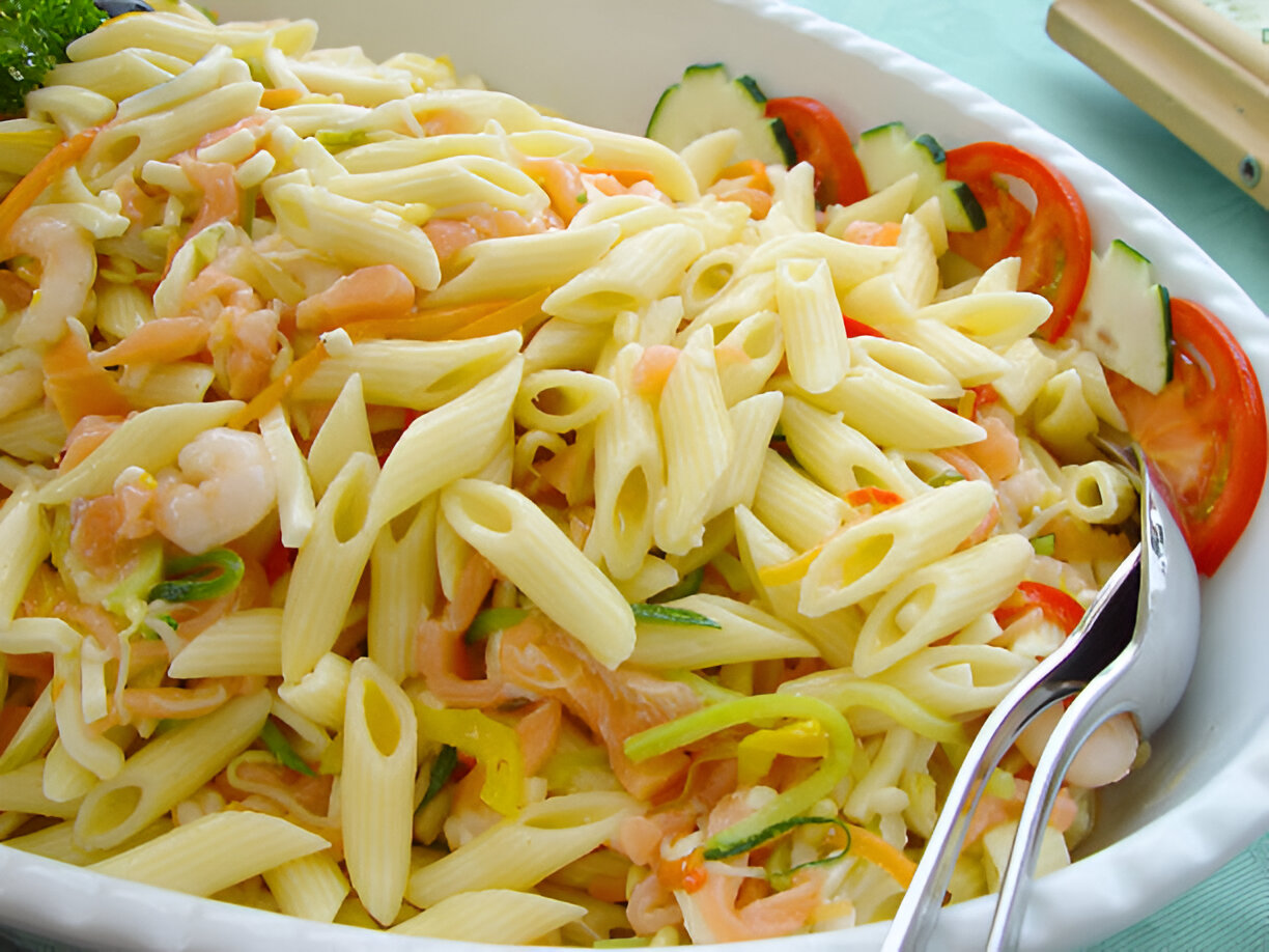 A serving of pasta salad featuring penne pasta, shrimp, and colorful vegetables like yellow bell peppers and tomatoes in a white bowl.