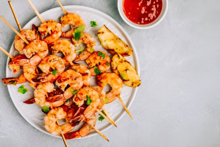 Grilled shrimp skewers served with grilled pineapple and dipping sauce on a white plate.