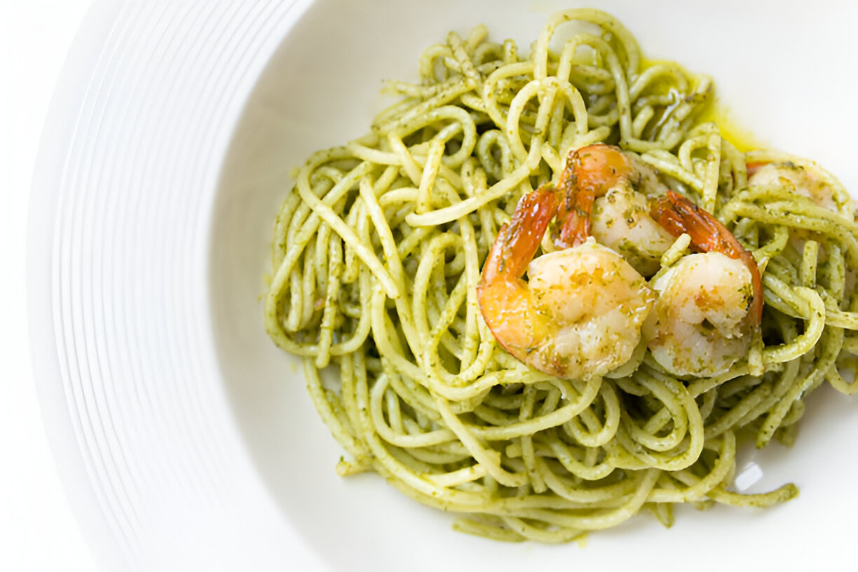 A plate of spaghetti with pesto sauce topped with shrimp.