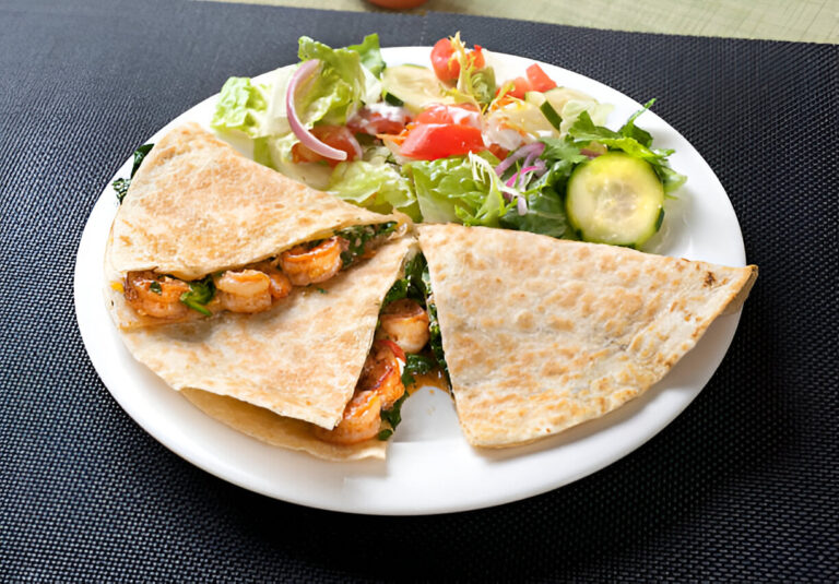 A plate with two shrimp-filled quesadillas and a side salad including greens, tomatoes, cucumbers, and onions.