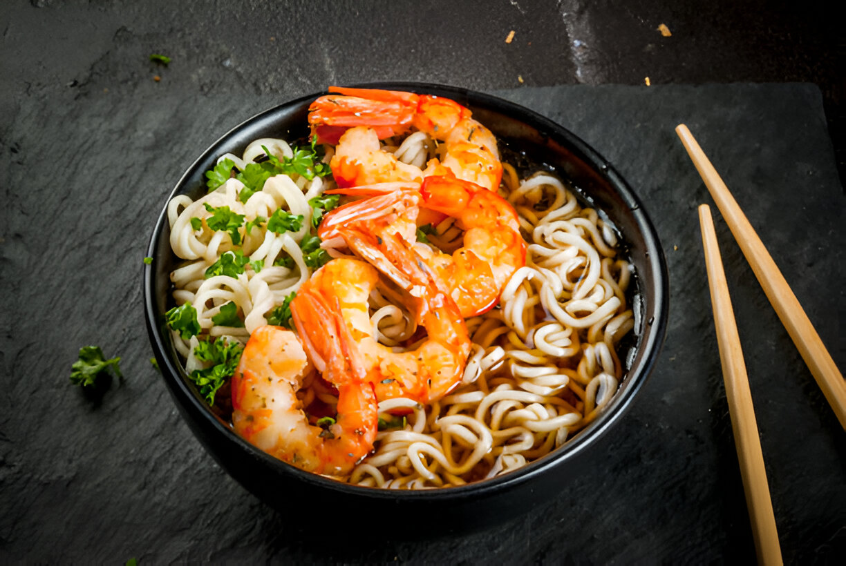 A bowl of shrimp ramen with noodles and parsley garnish on a dark textured surface.