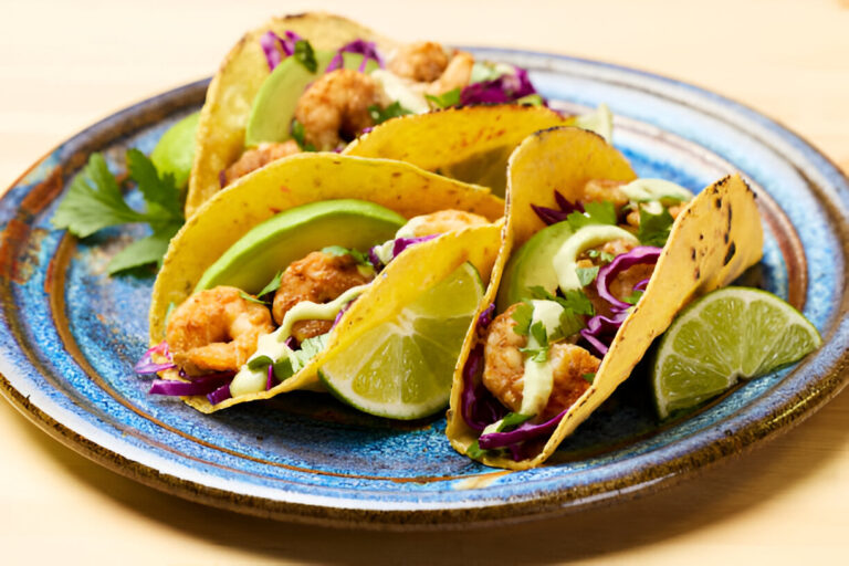 Three shrimp tacos with toppings on a blue plate