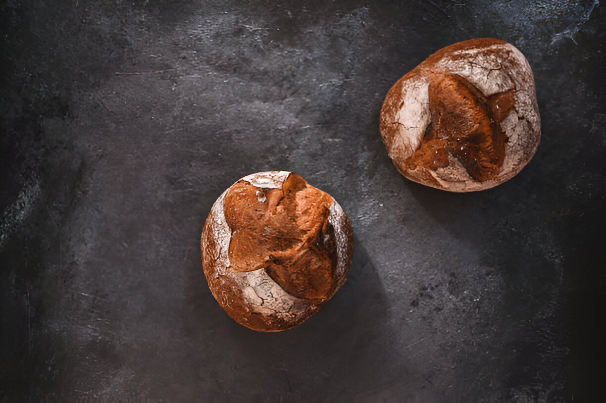 Two round rustic bread rolls with a flour dusting on a dark background.
